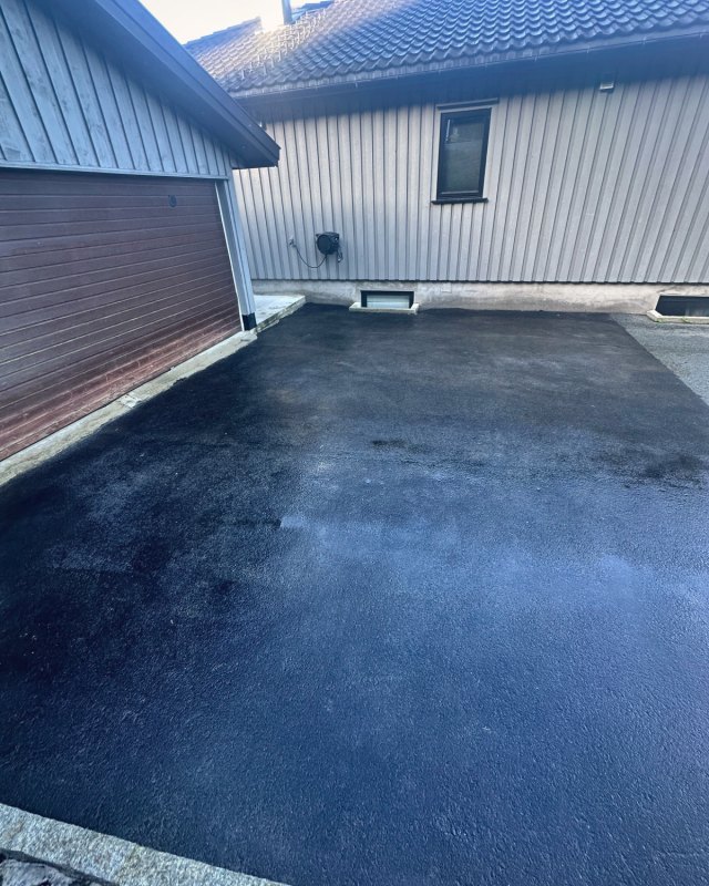Innkjørsel foran garasje og hus med nyfornyet, dyp svart asfalt.